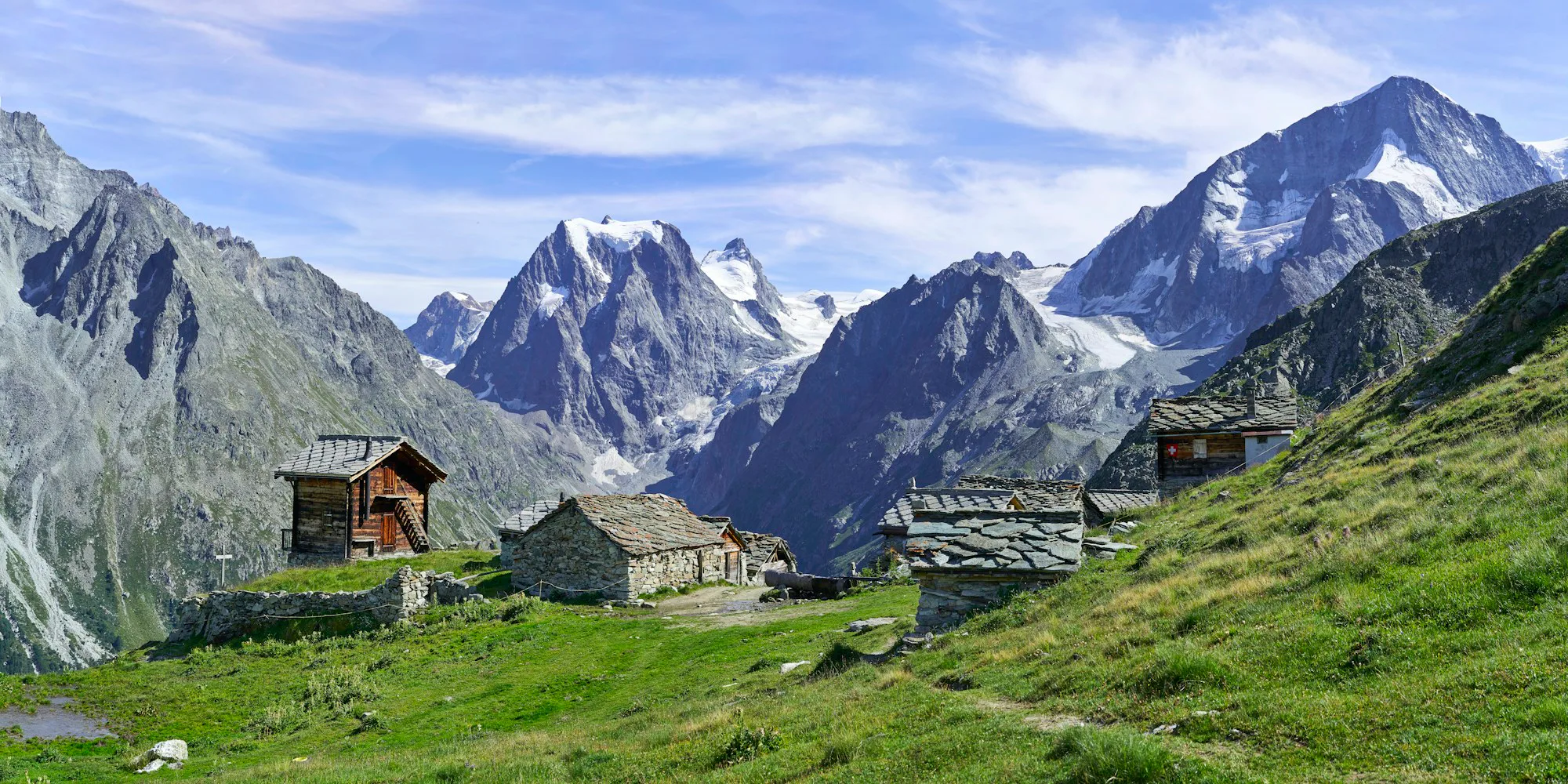 Stone and timber huts in an alpine pasture below snowy peaks