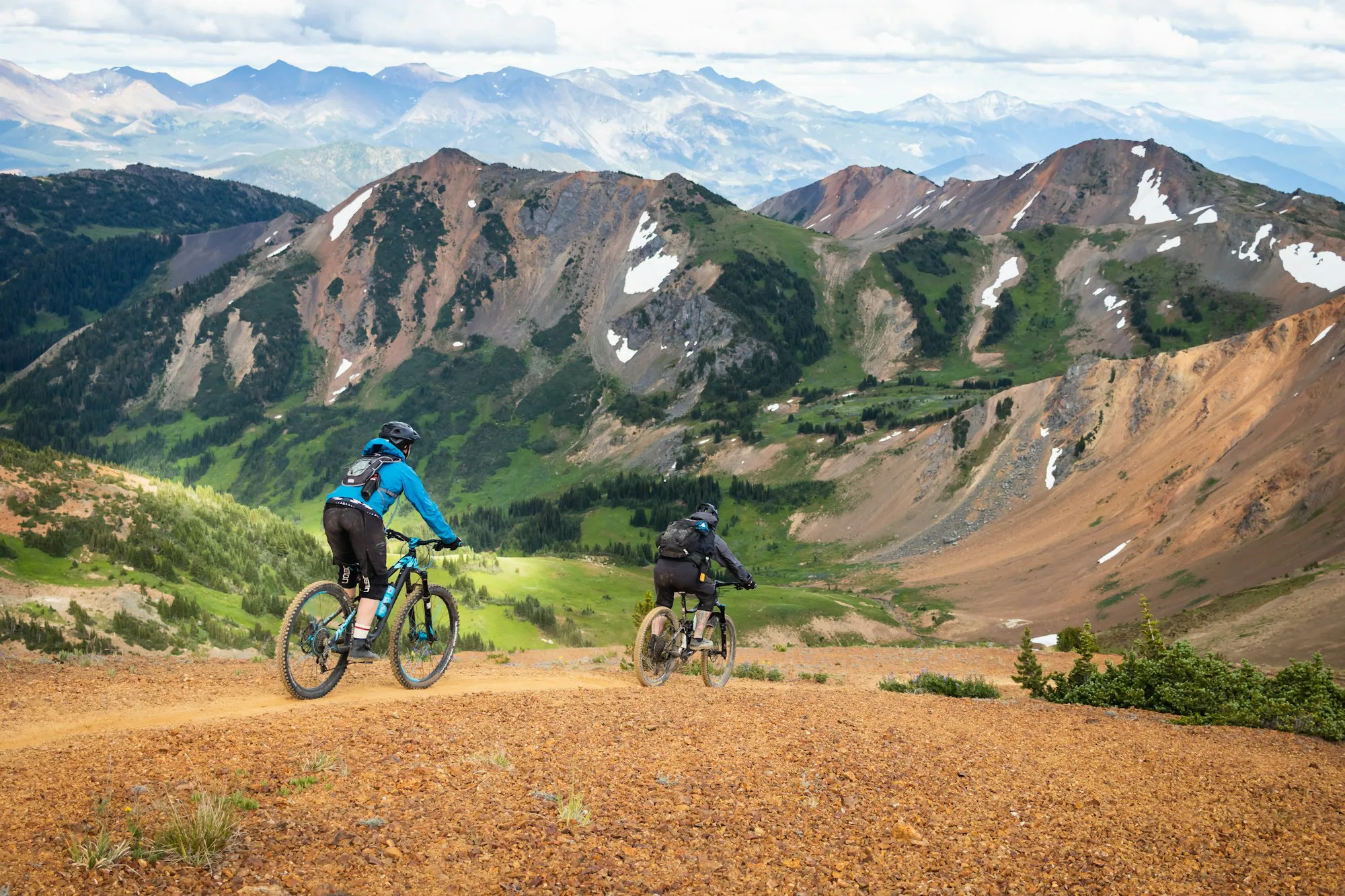Two riders on a dirt road among colourful mountains