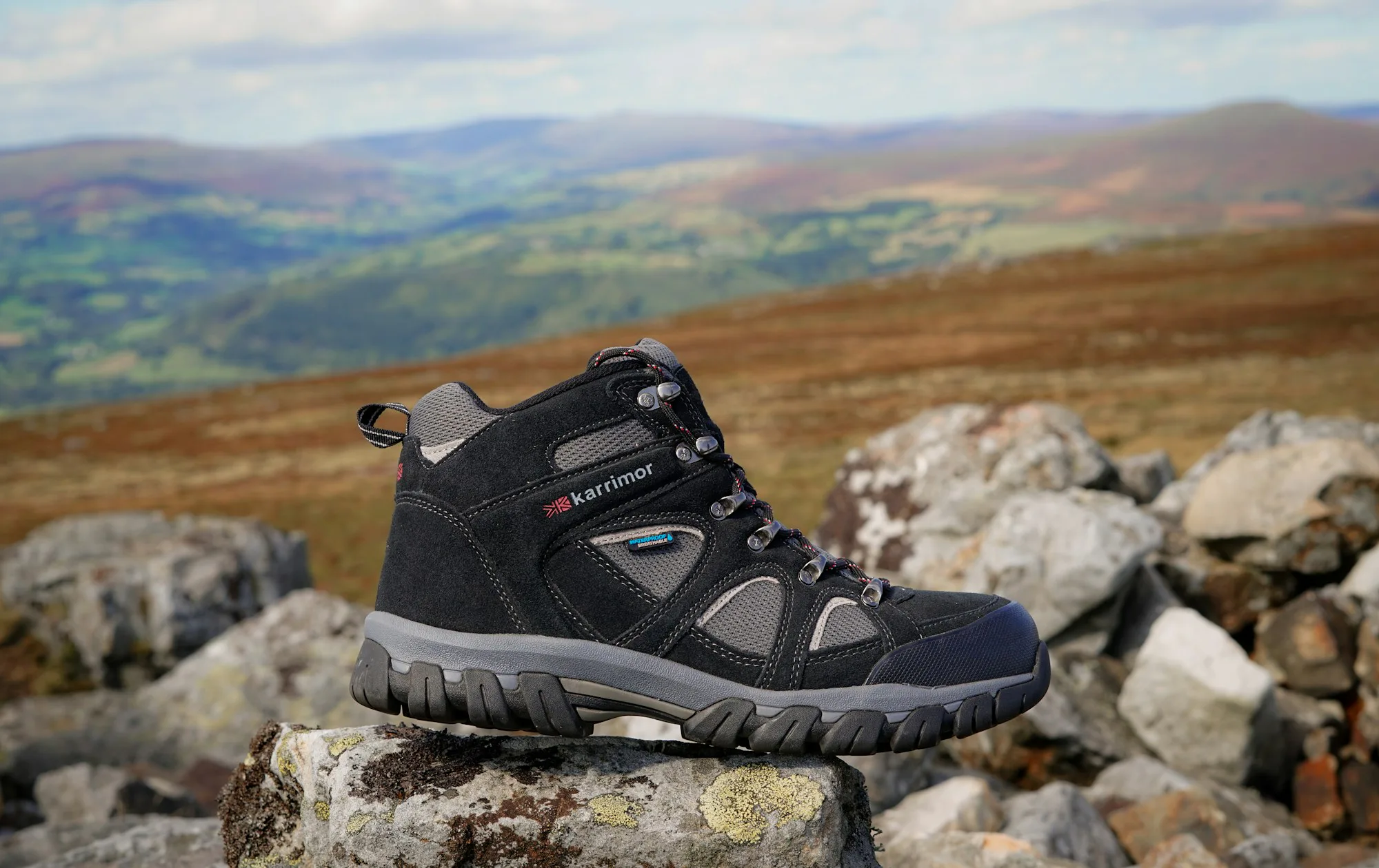 A mid-height hiking boot on rocks above rolling hills