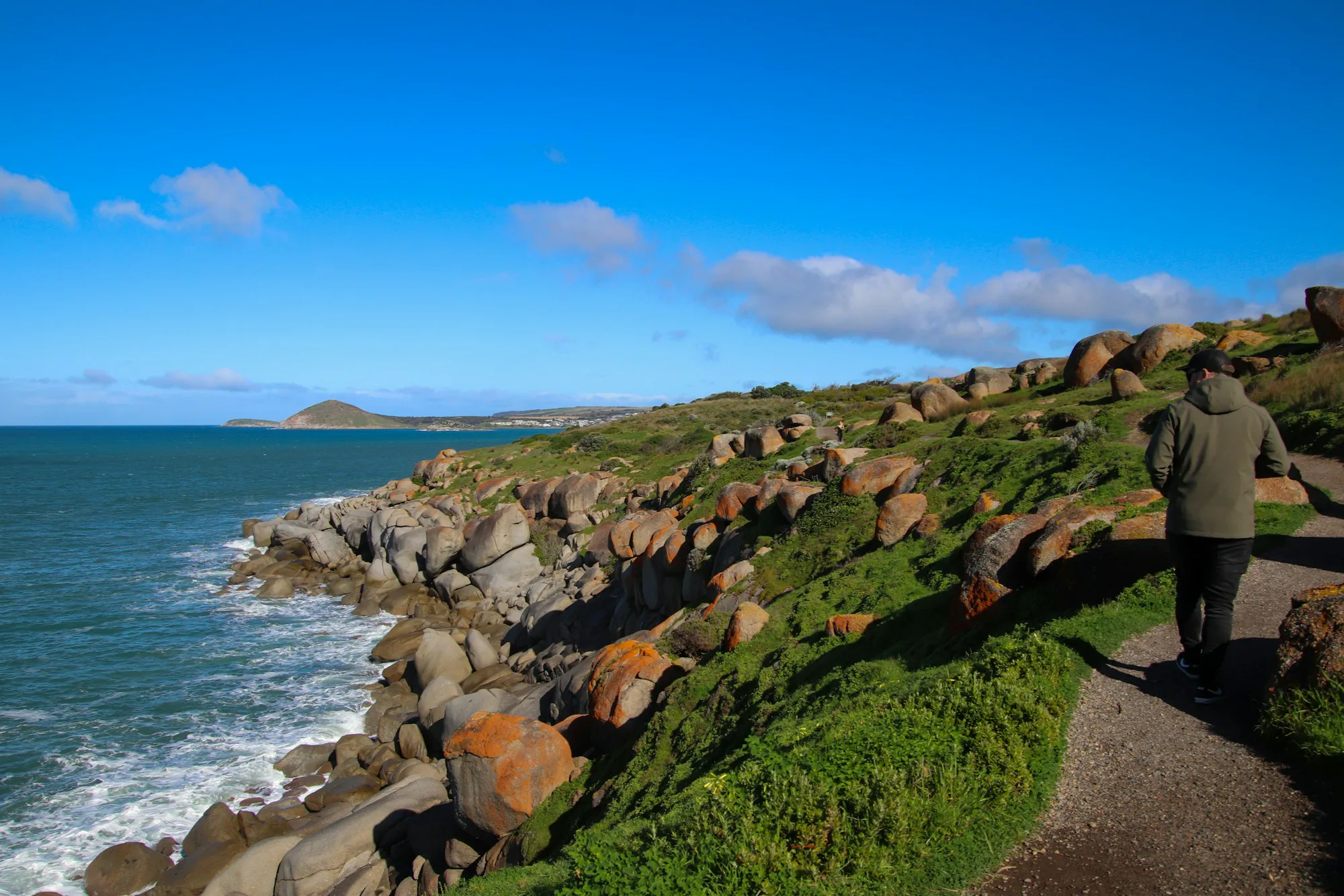 A person walking along a path beside the ocean