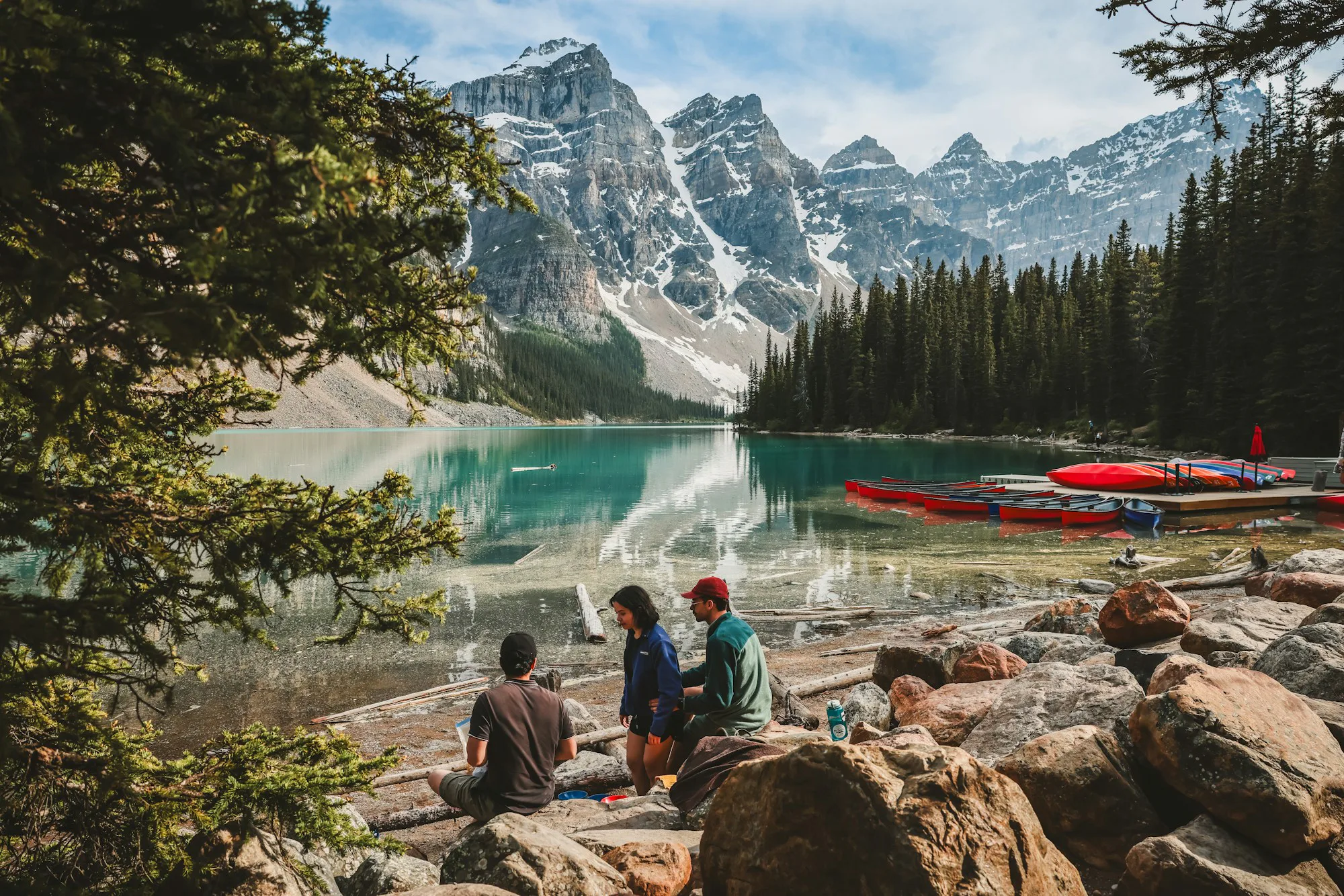 Families resting by a turquoise lake with canoes on the shore