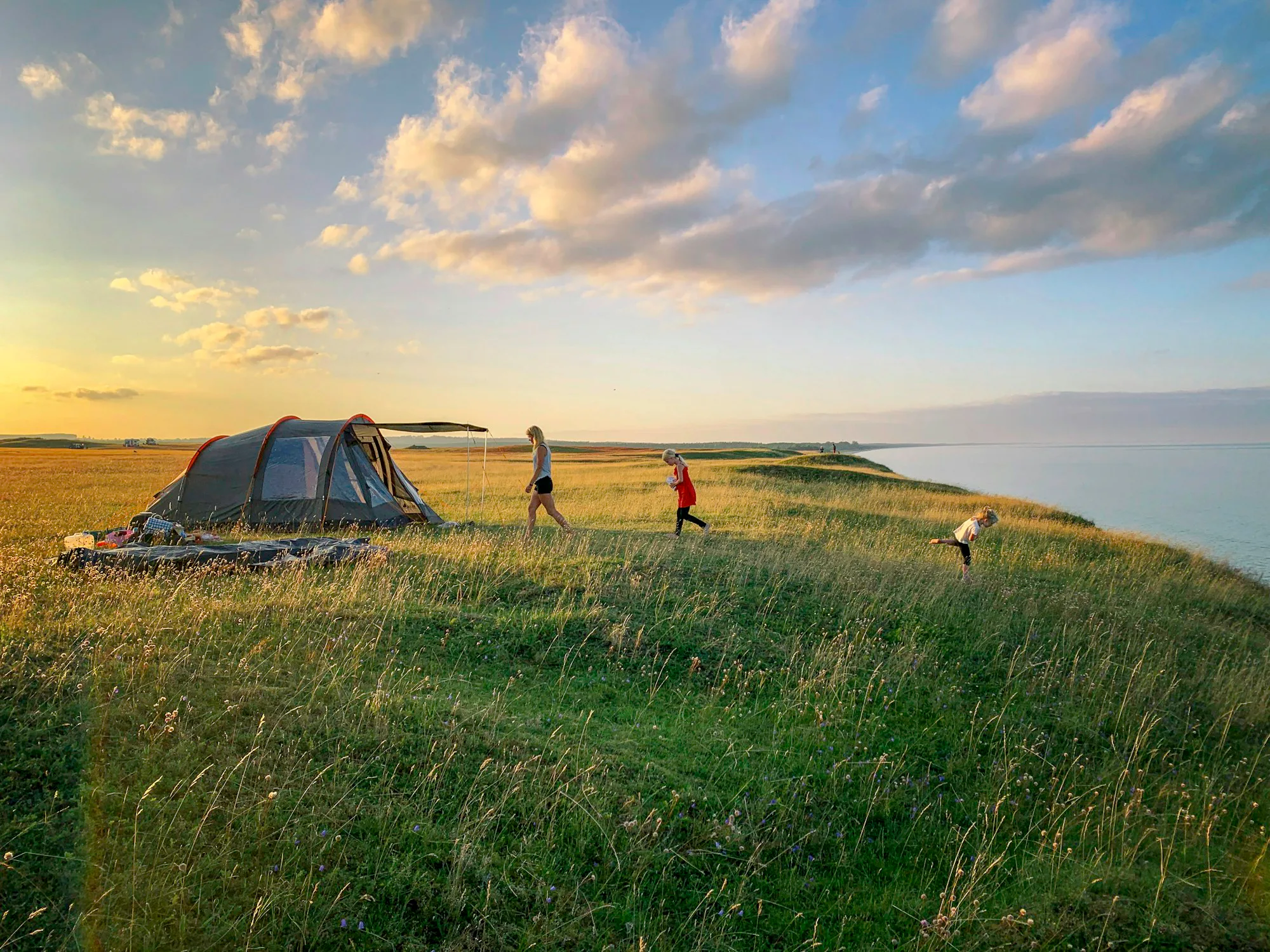 A toddler walking on the grass beside a tent in evening light