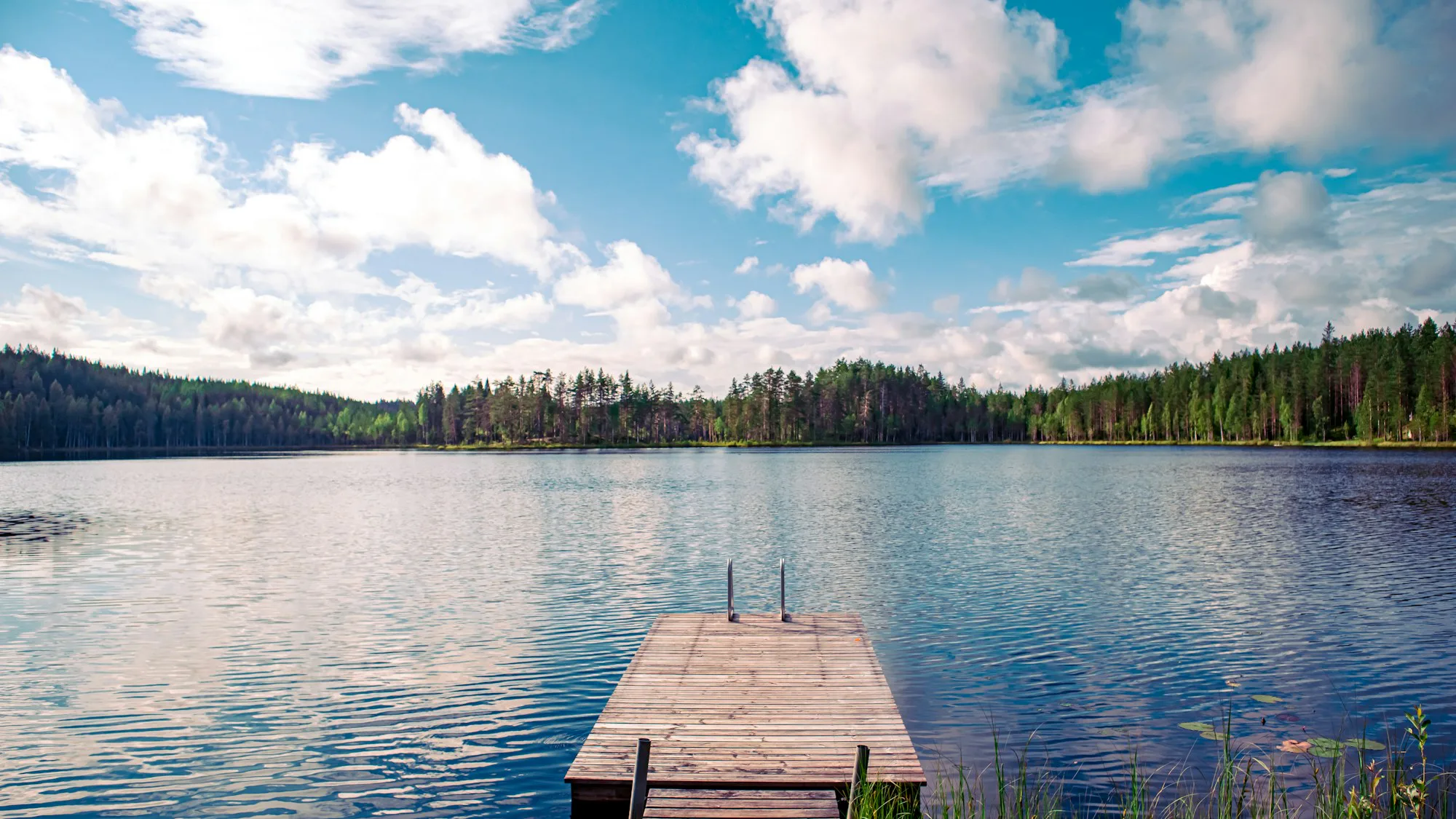 A wooden jetty reaching into a calm lake under a blue sky