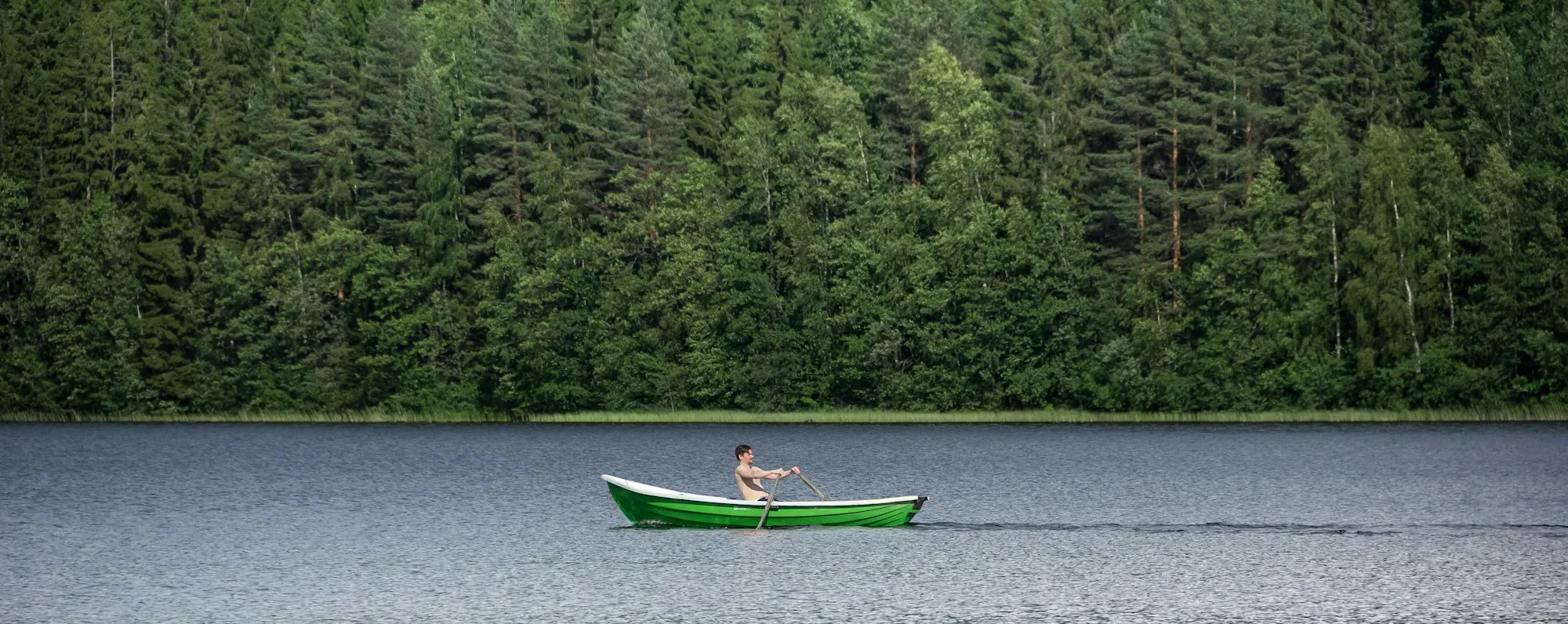 A paddler in a green canoe on a forest lake