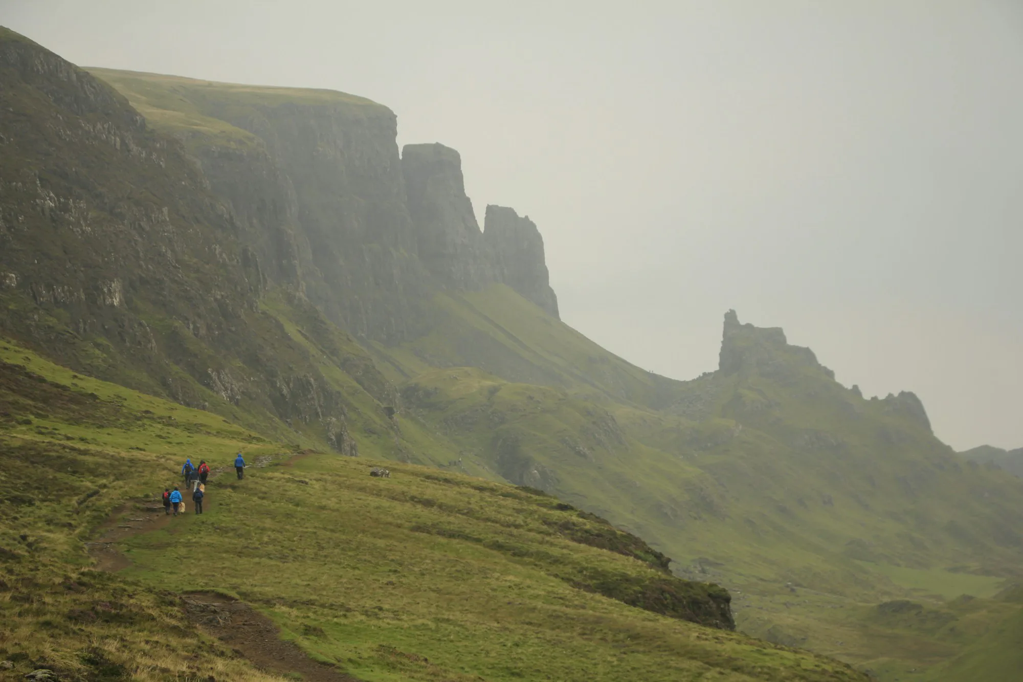 A group of people hiking up a grassy hill