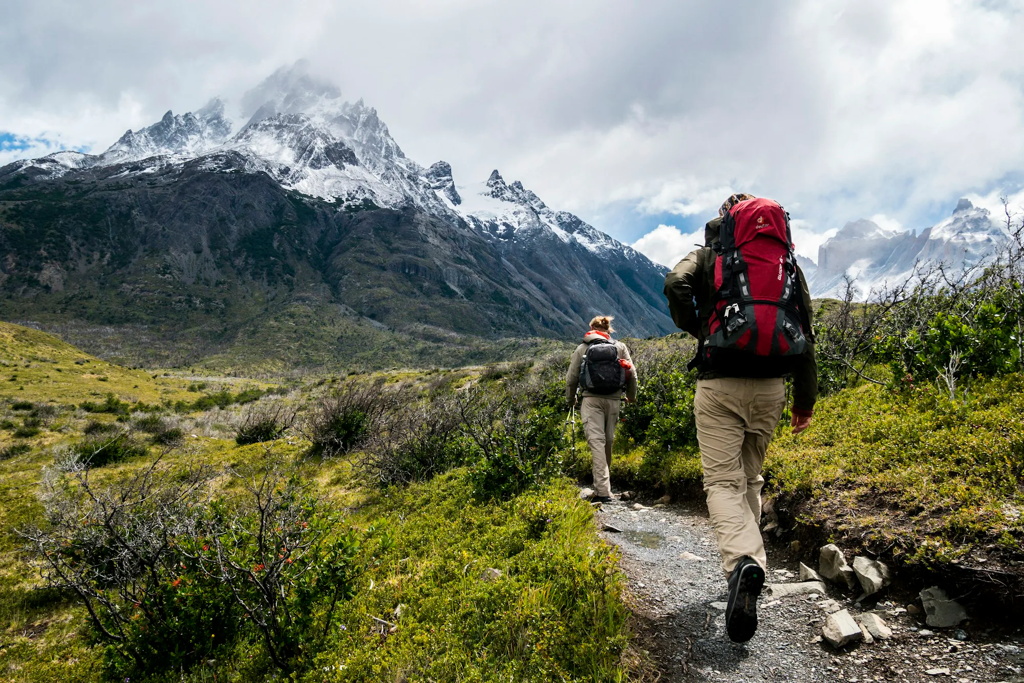 Two hikers with backpacks walking towards snow-capped mountains