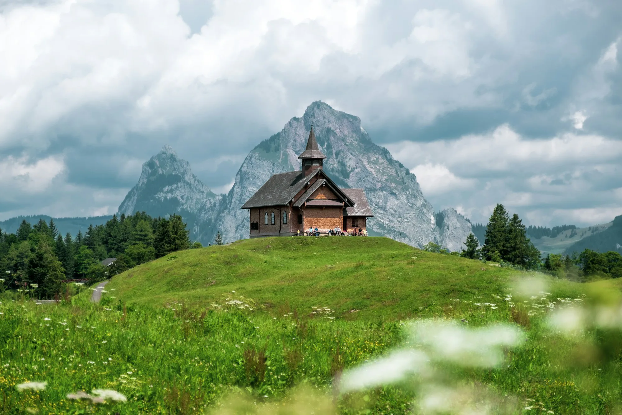 A wooden mountain hut on a green meadow below rocky peaks