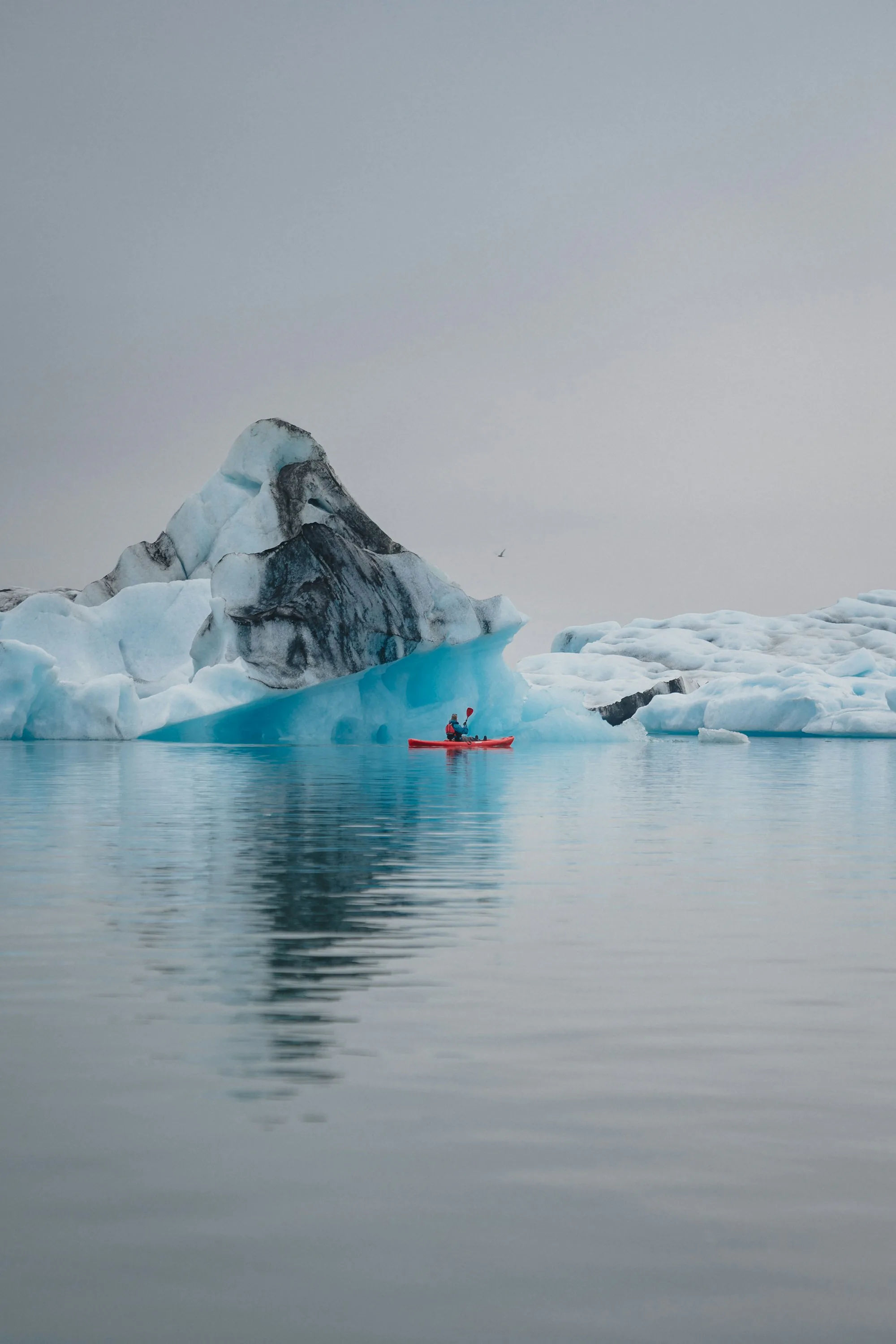 A kayaker paddling past a blue iceberg on a glacier lagoon