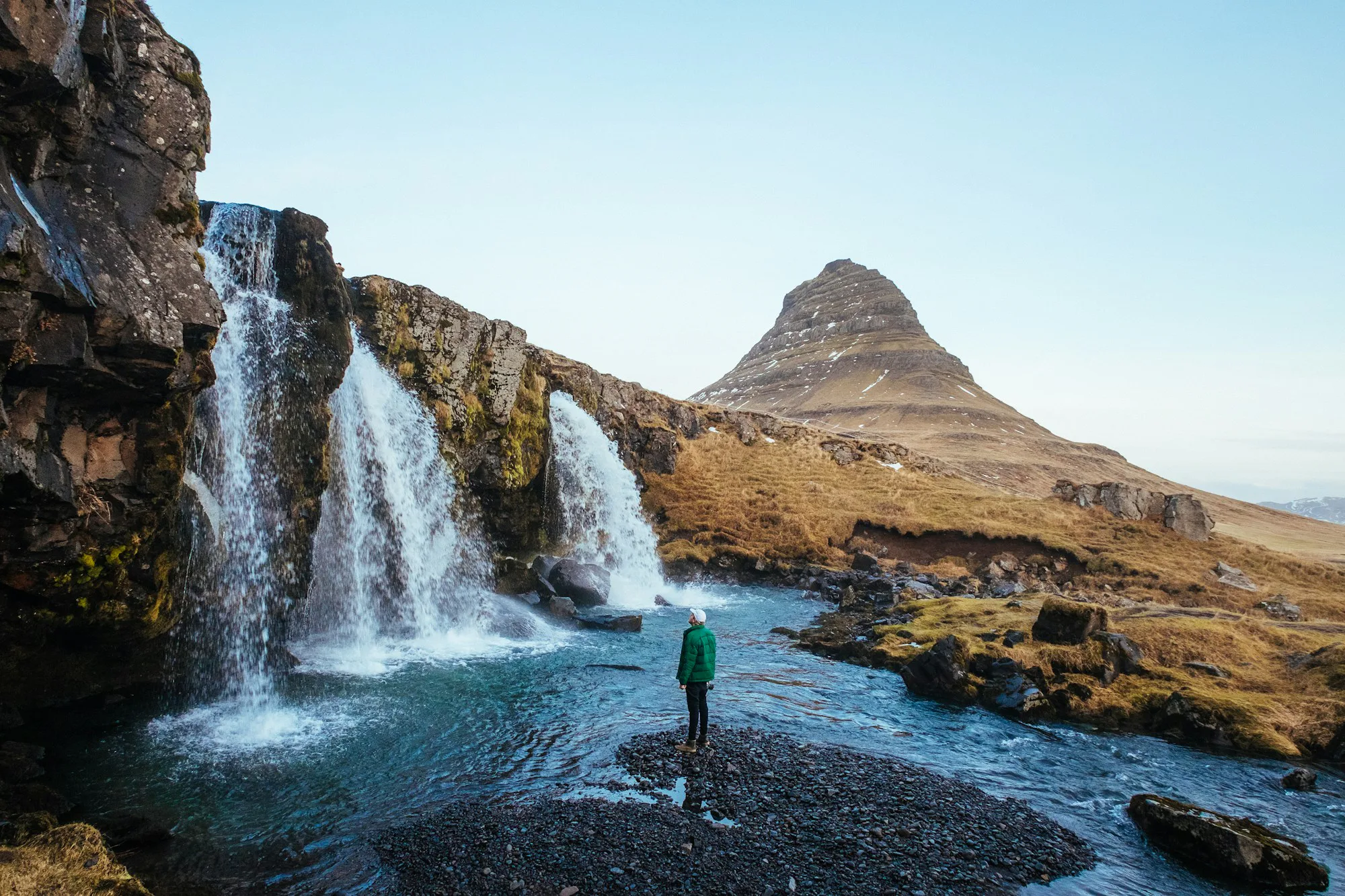 A hiker by waterfalls below the peak of Kirkjufell