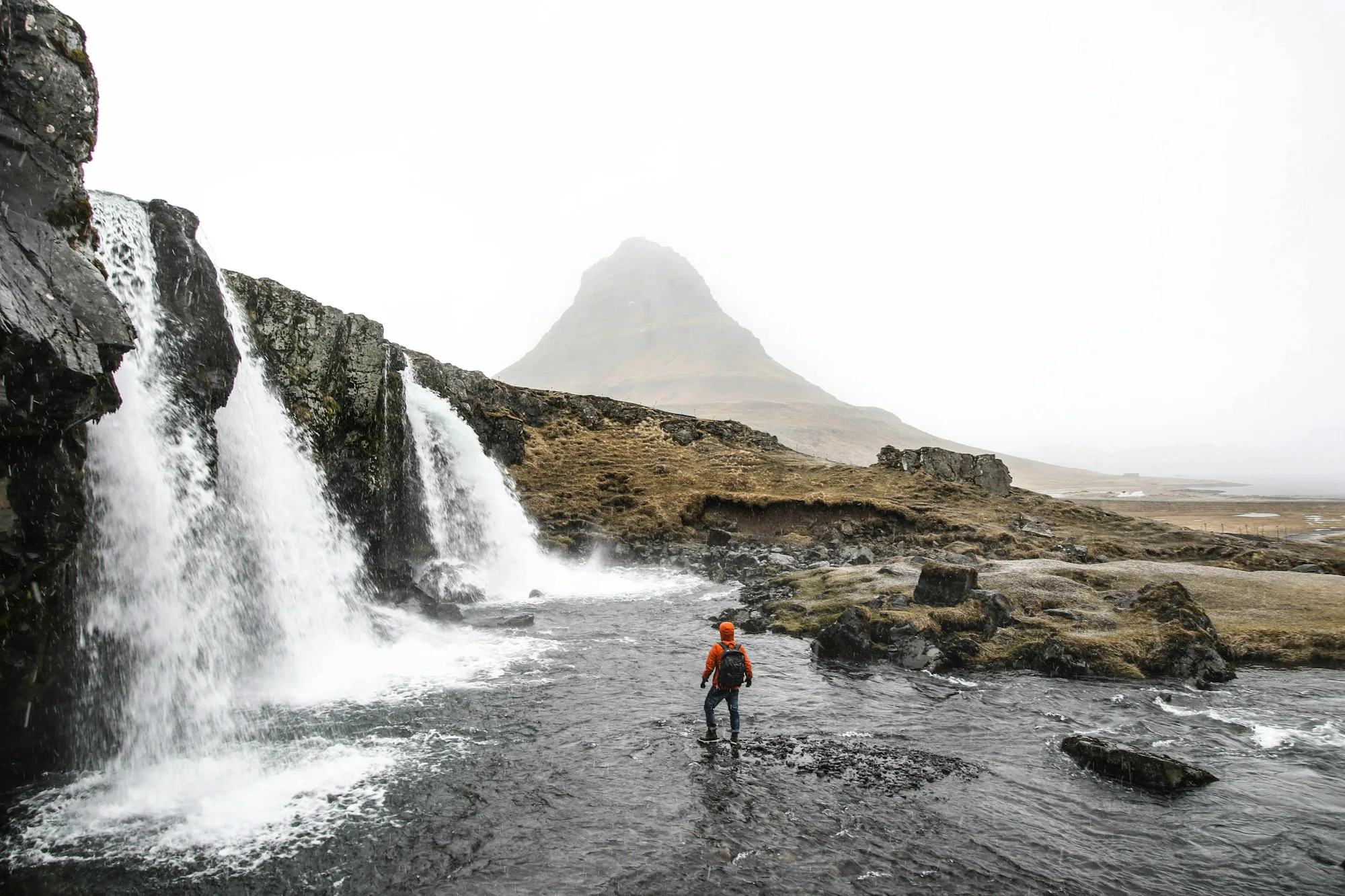 A walker crossing the river below Kirkjufellsfoss waterfalls