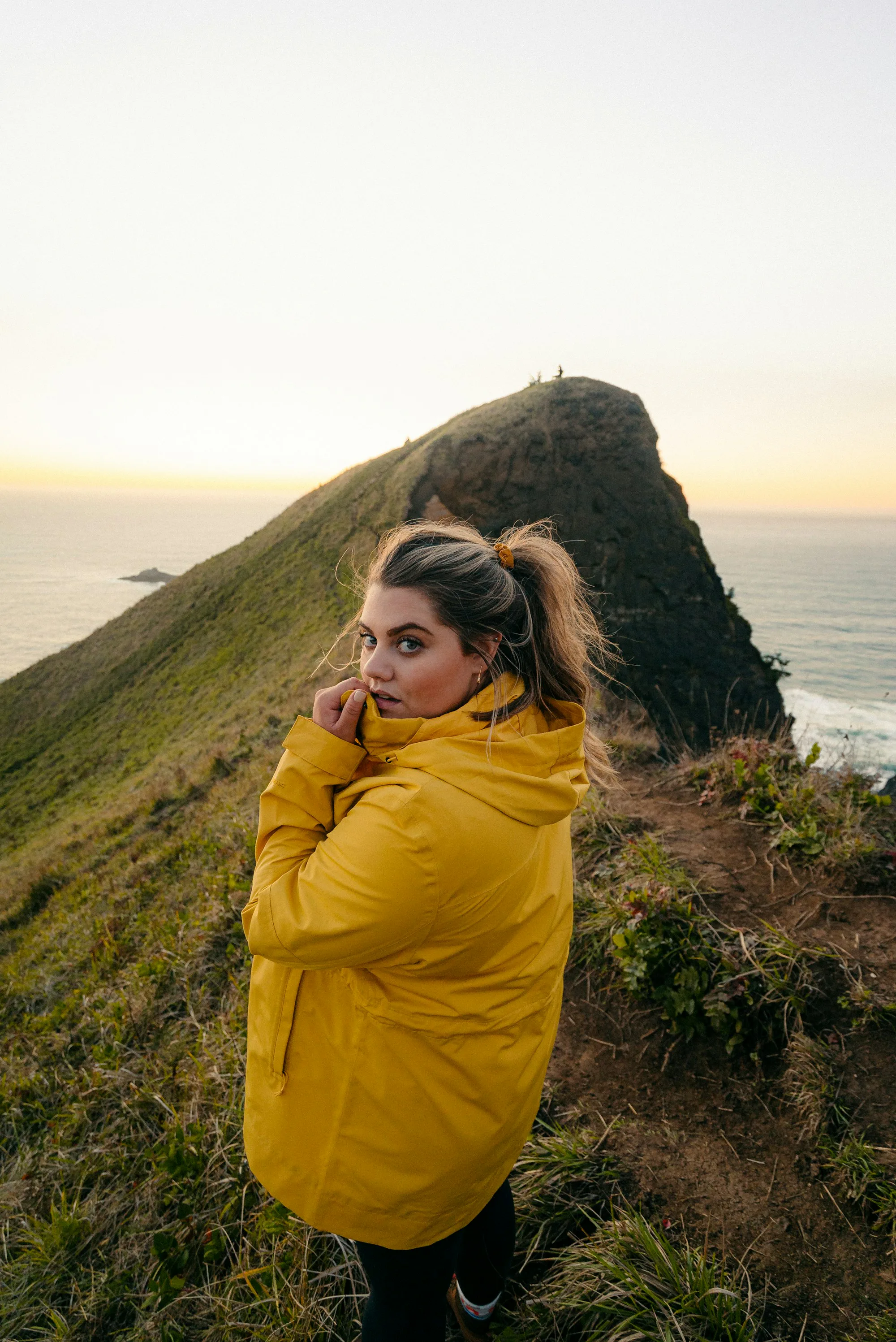 A woman in a yellow jacket on a green ridge above the sea
