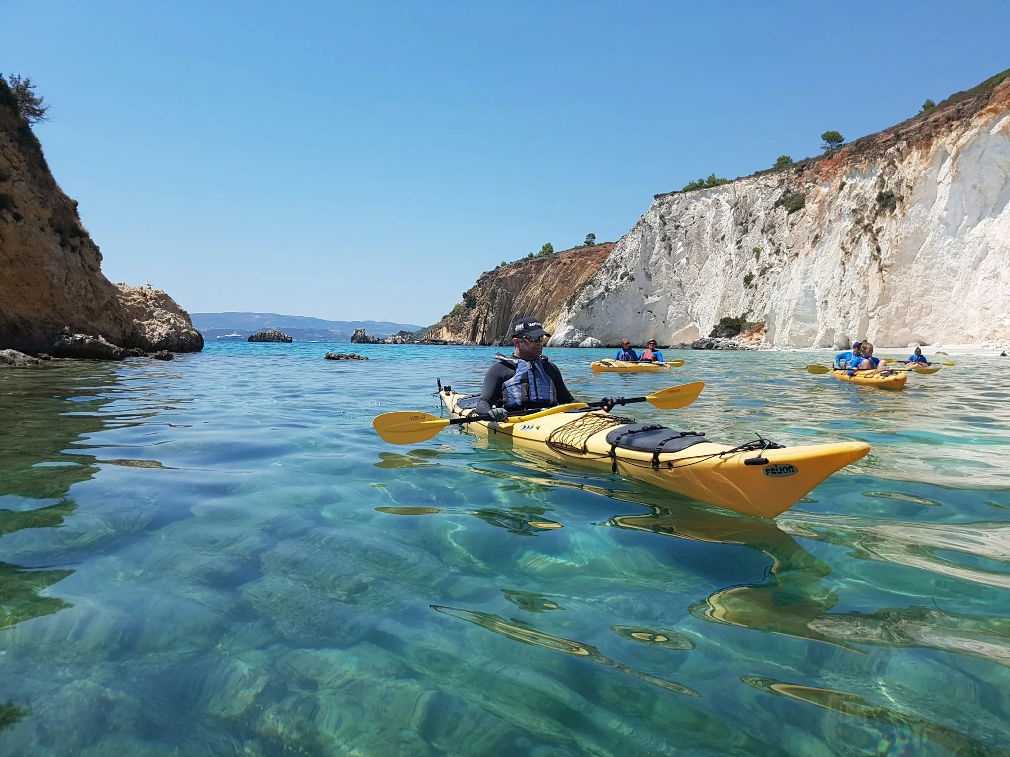 Kayakers paddling across clear blue water below white cliffs