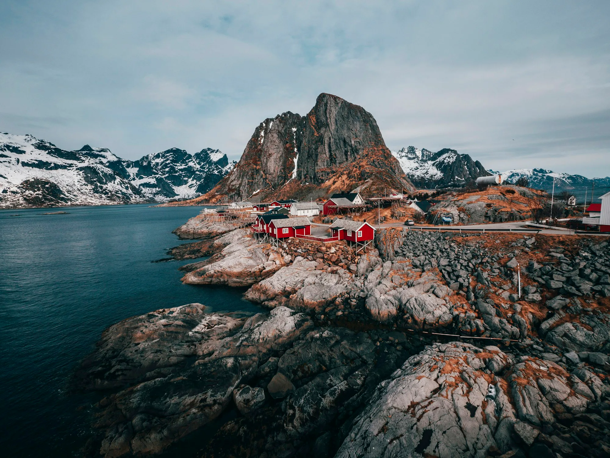 Red cabins on a rocky shore beneath snow-capped mountains in Lofoten