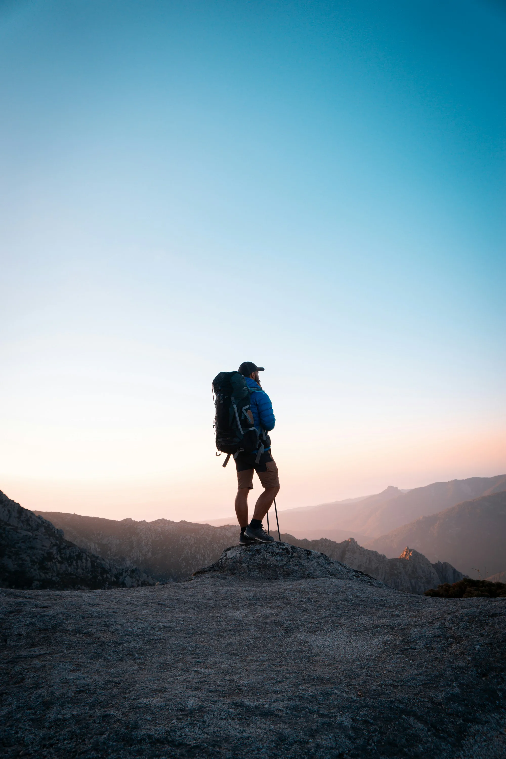 A hiker with a large backpack on a rocky peak at golden hour