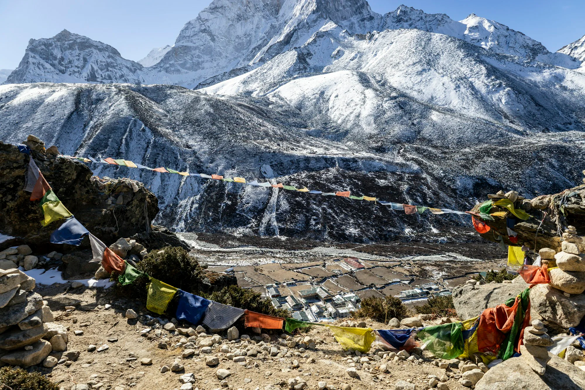 Prayer flags along a rocky trail below a snow-capped peak