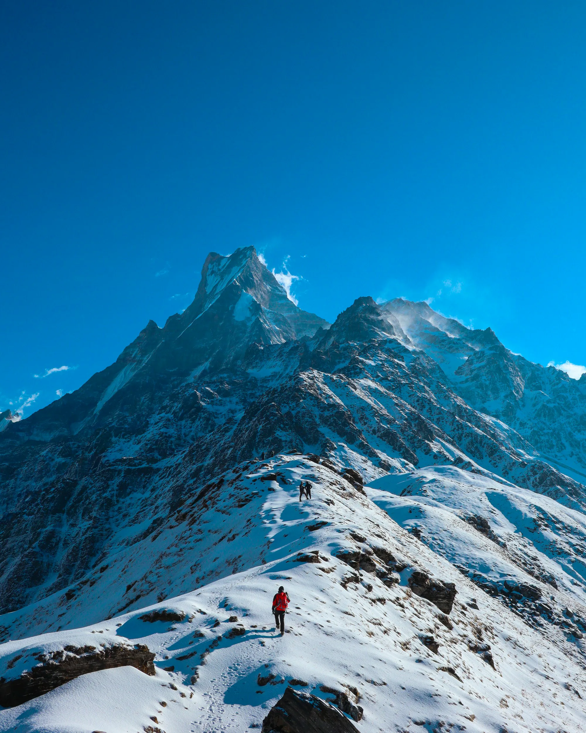 Trekkers on a snowy ridge below the fishtail peak of Machapuchare