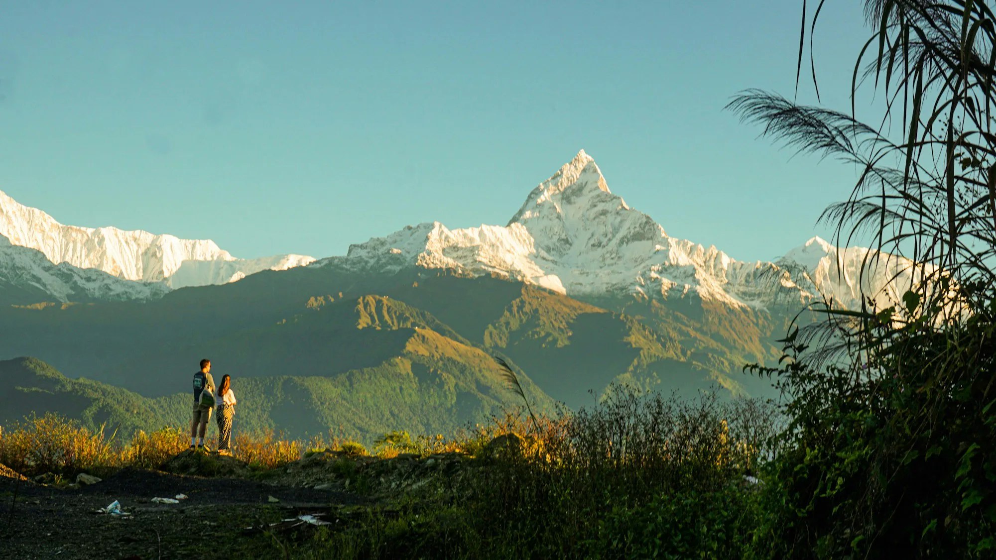 Two trekkers on a green hillside below the fishtail peak of Machapuchare