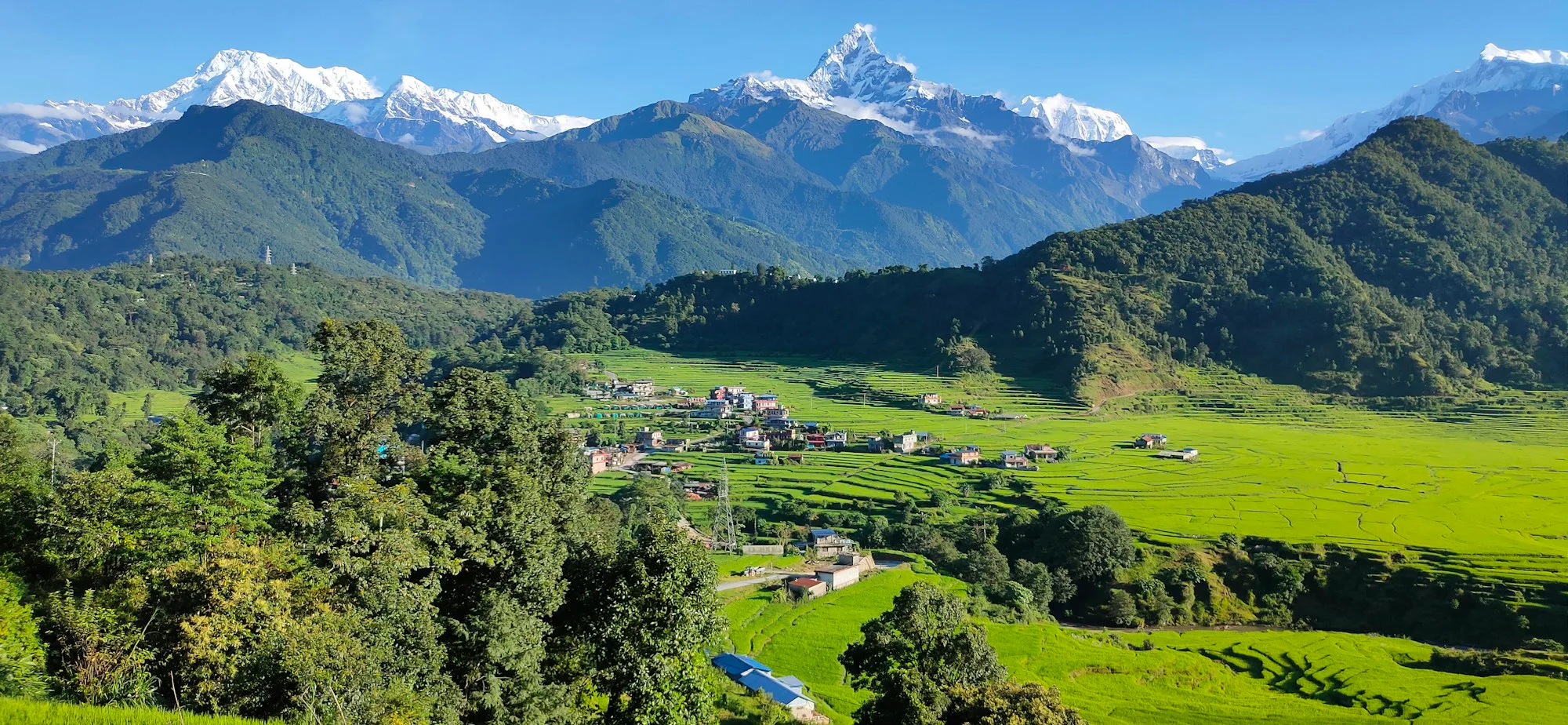Green fields and a village in a valley below snowy peaks