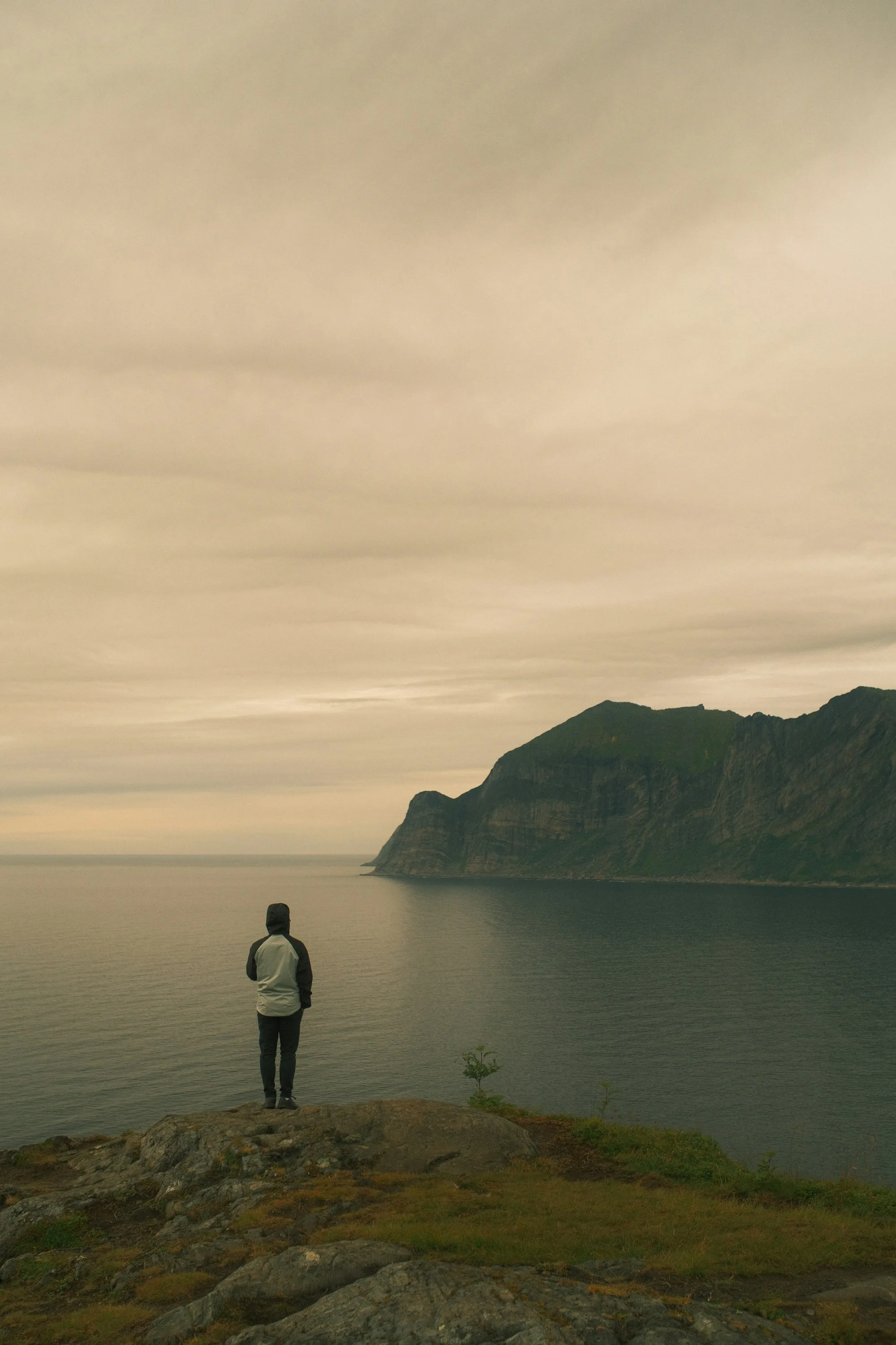 A walker on a clifftop looking over the sea to distant mountains