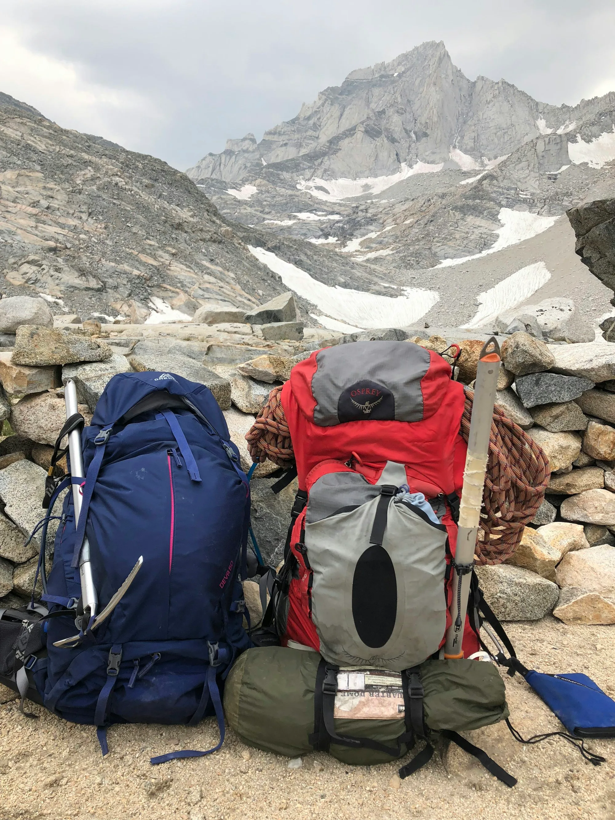 Two packed rucksacks, a rope and an ice axe on a rocky mountain path