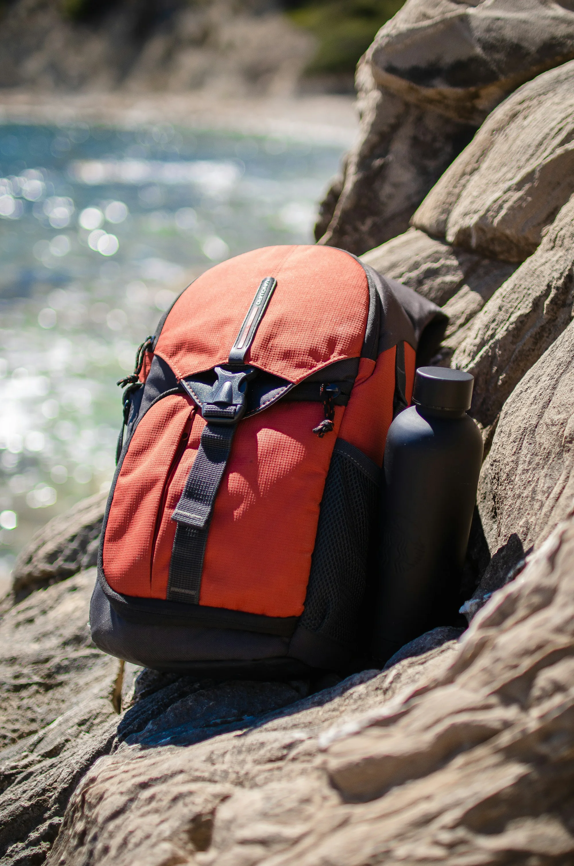A red daypack and water bottle on a rock
