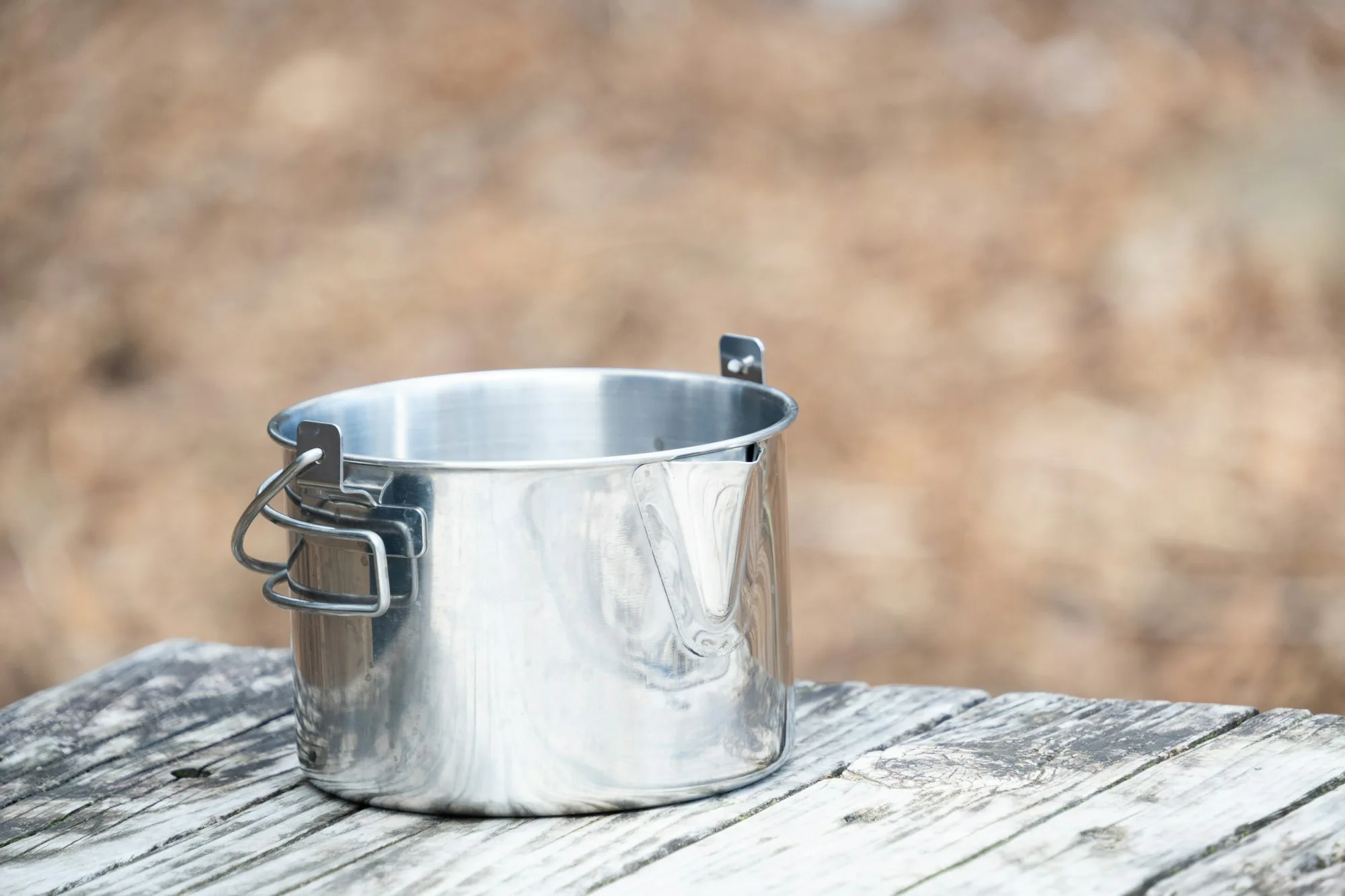 A steel camping pot with a handle on a wooden table