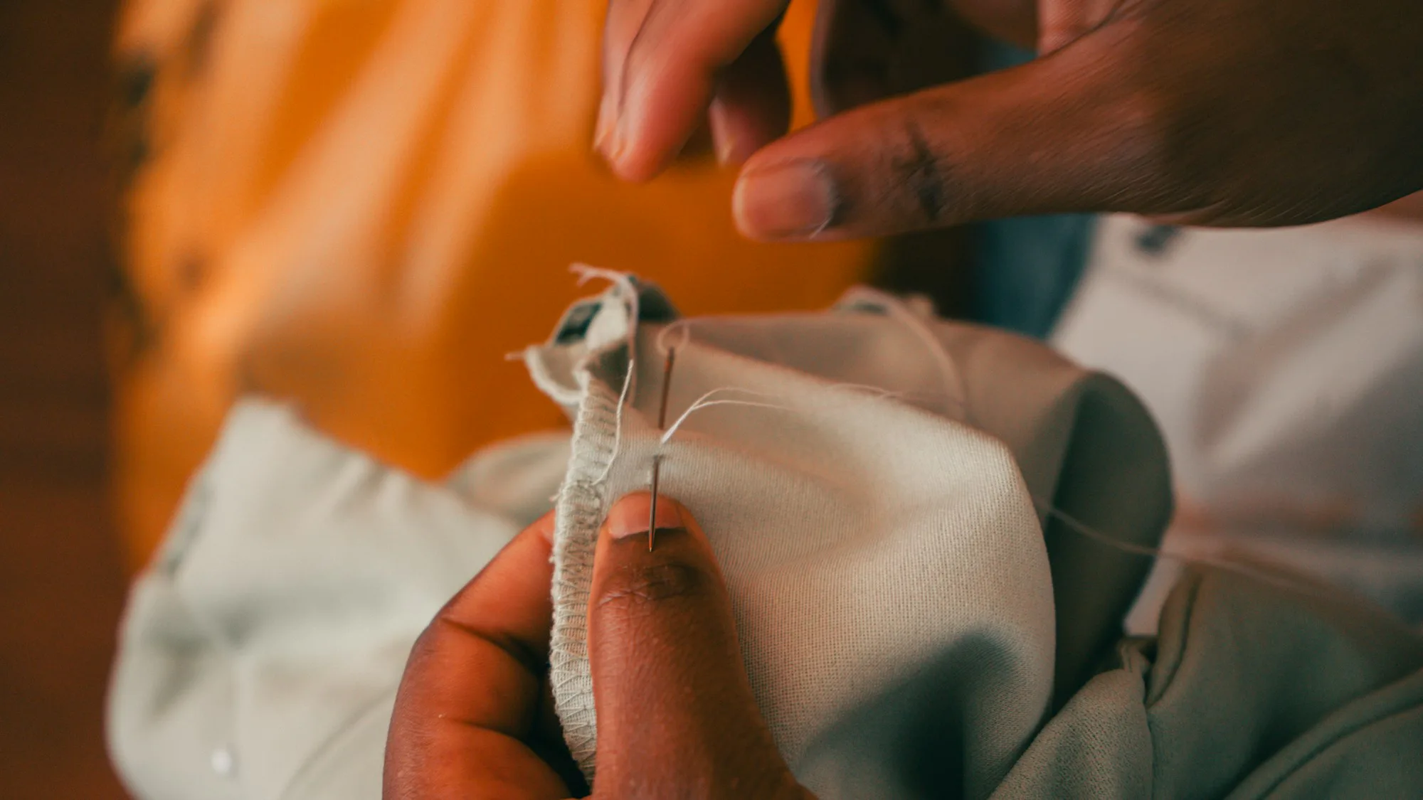 Hands stitching a repair into orange fabric with needle and thread