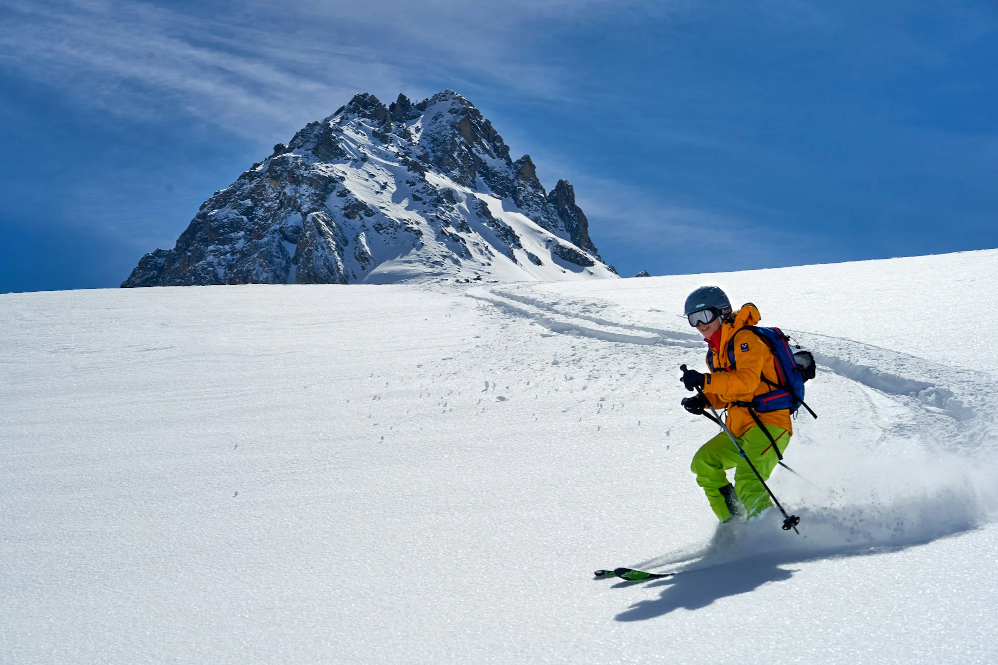 A skier in an orange jacket below a rocky peak