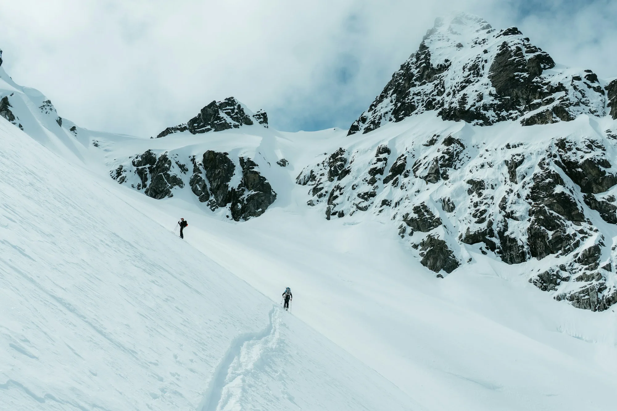 Two ski tourers climbing a steep snowy mountainside