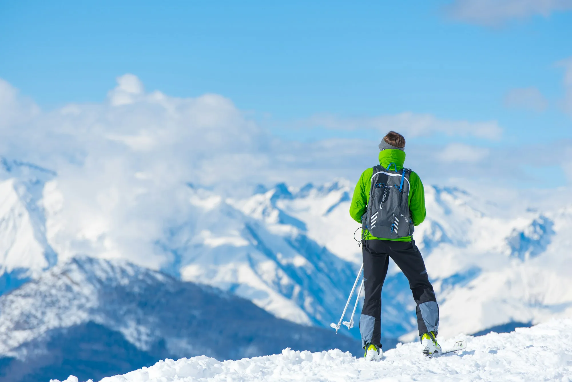 A ski tourer in a green jacket on a summit above the clouds
