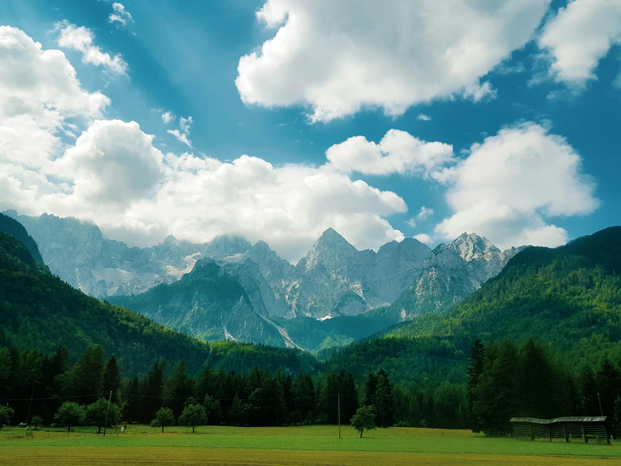 Green forests and peaks of the Julian Alps under white clouds