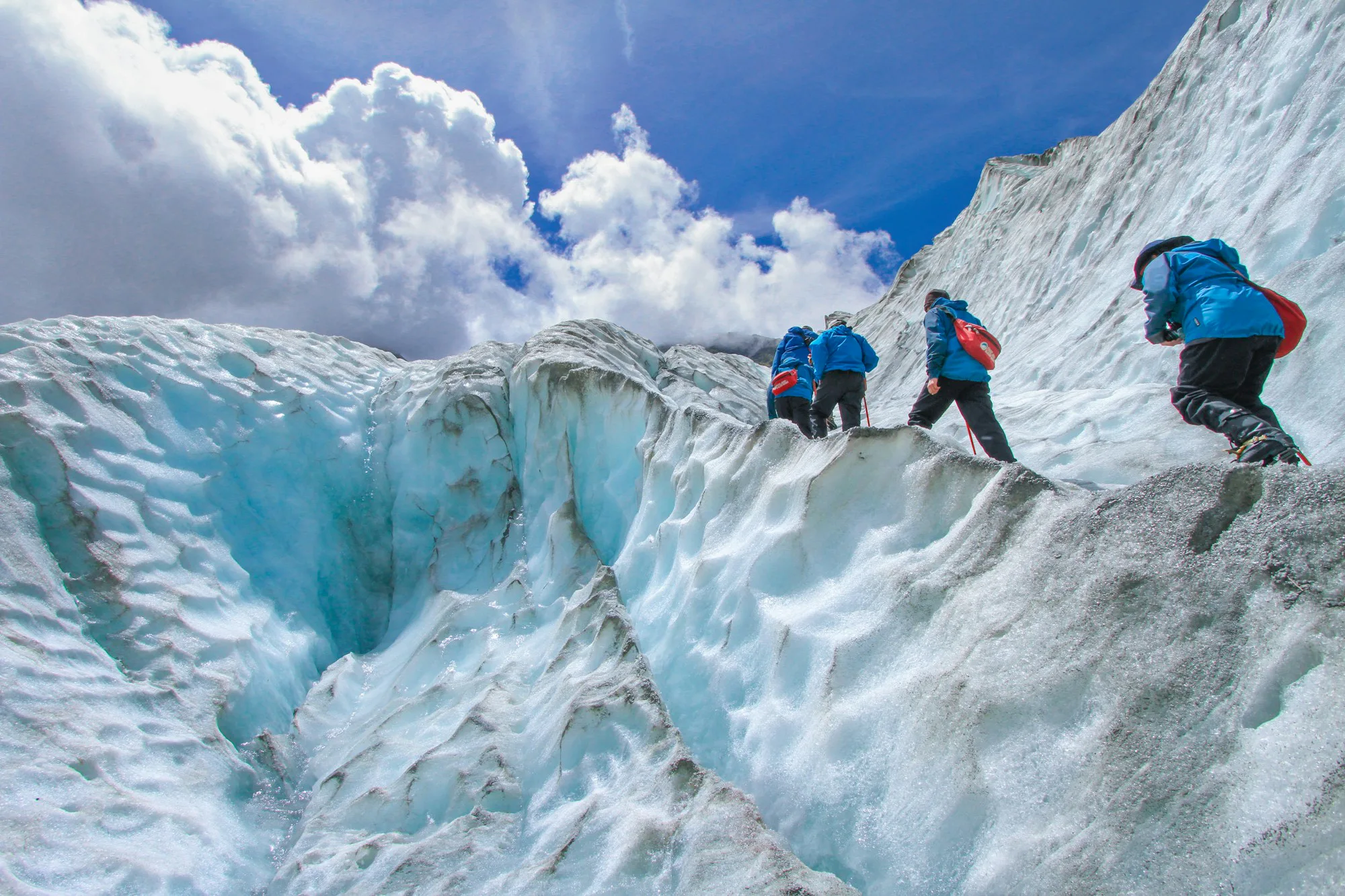 Climbers with crampons and ropes on a blue glacier ice wall