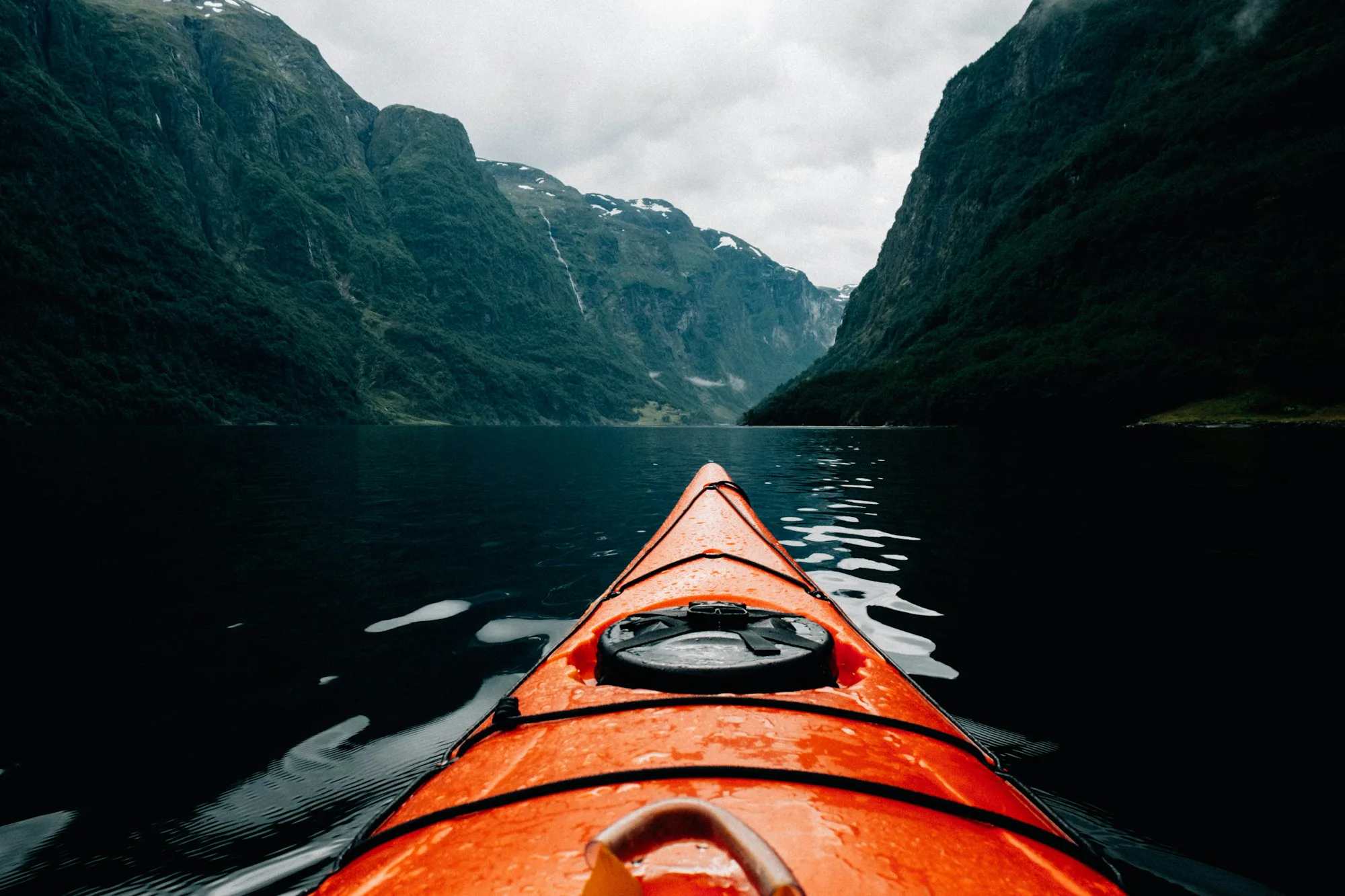 Looking over the bow of an orange kayak towards the mouth of a fjord