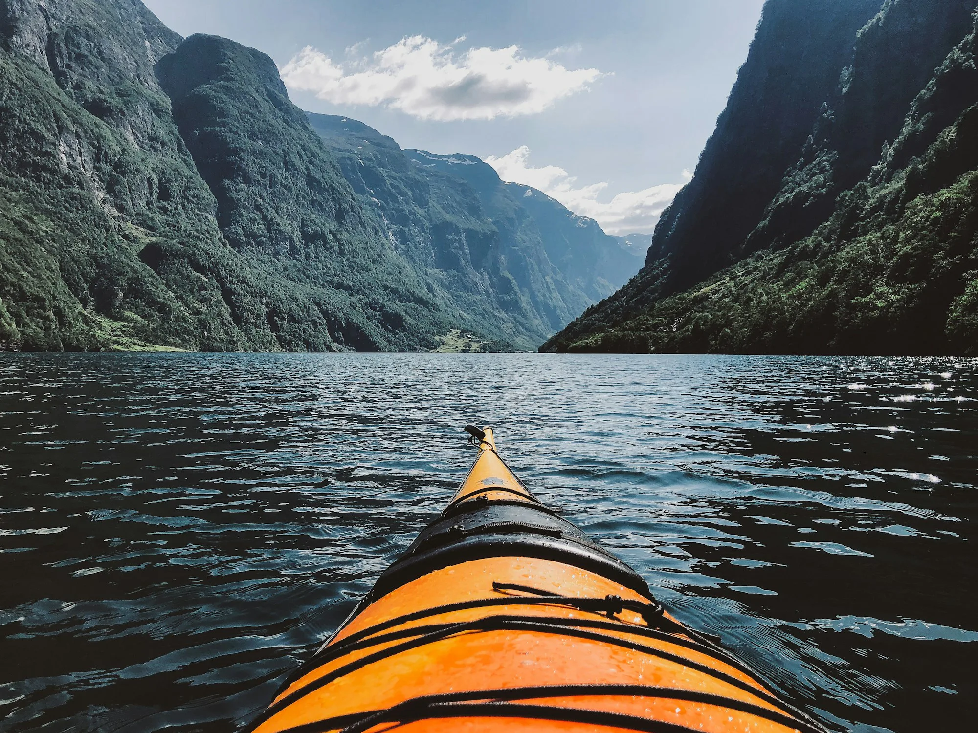 The bow of an orange kayak on a fjord between steep mountains