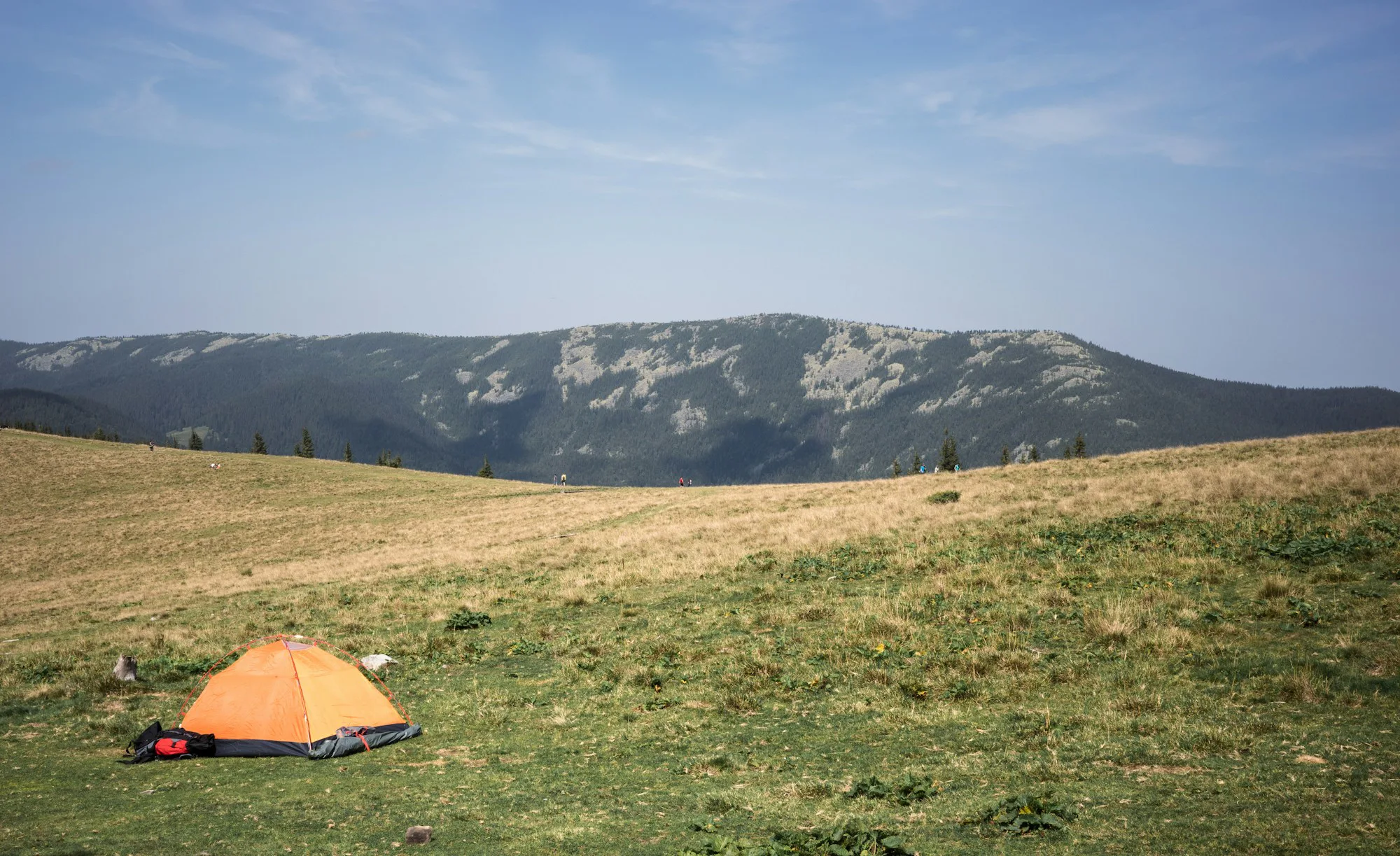 A small orange tent pitched on open grassland below hills