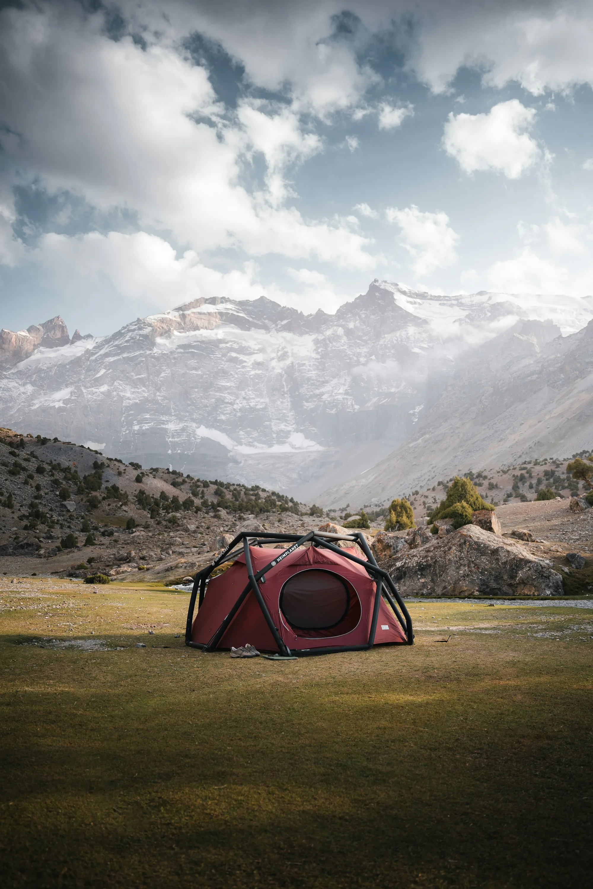 A red tent in a valley below snowy mountains