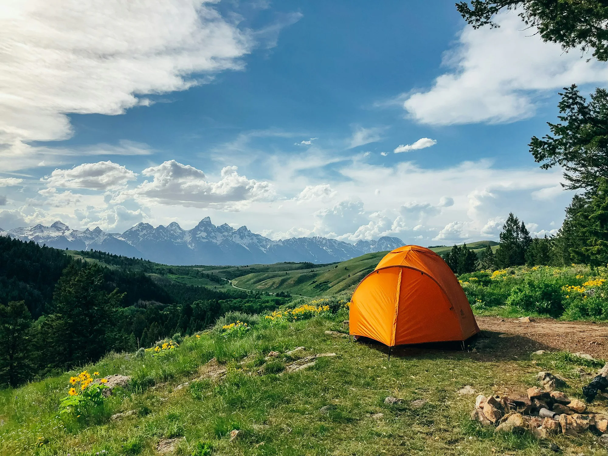An orange tent in a green valley below mountains