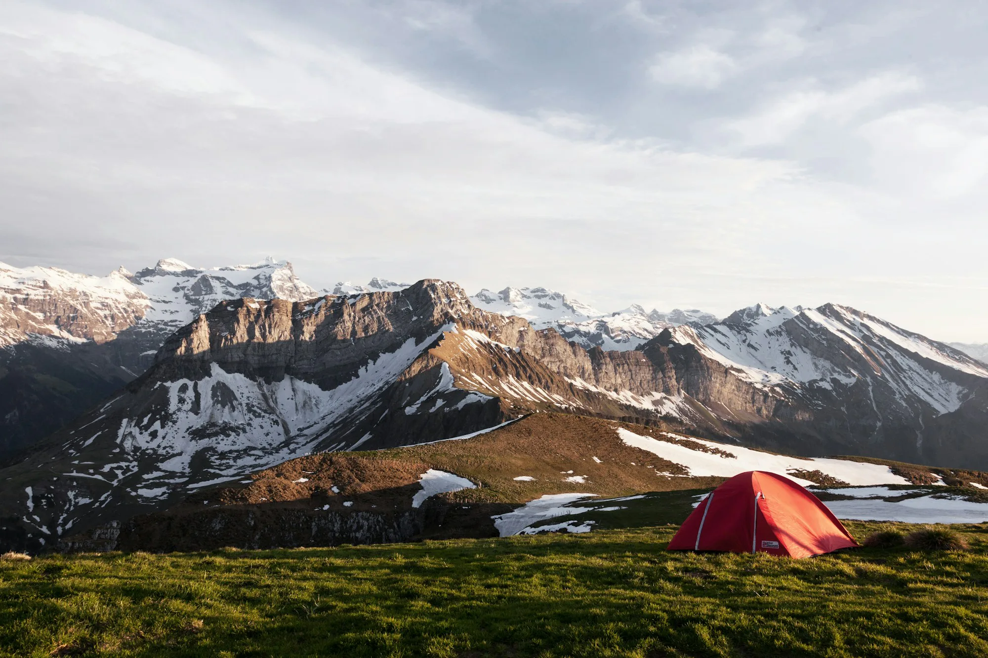 A red tent on a grassy field below snow-capped mountains