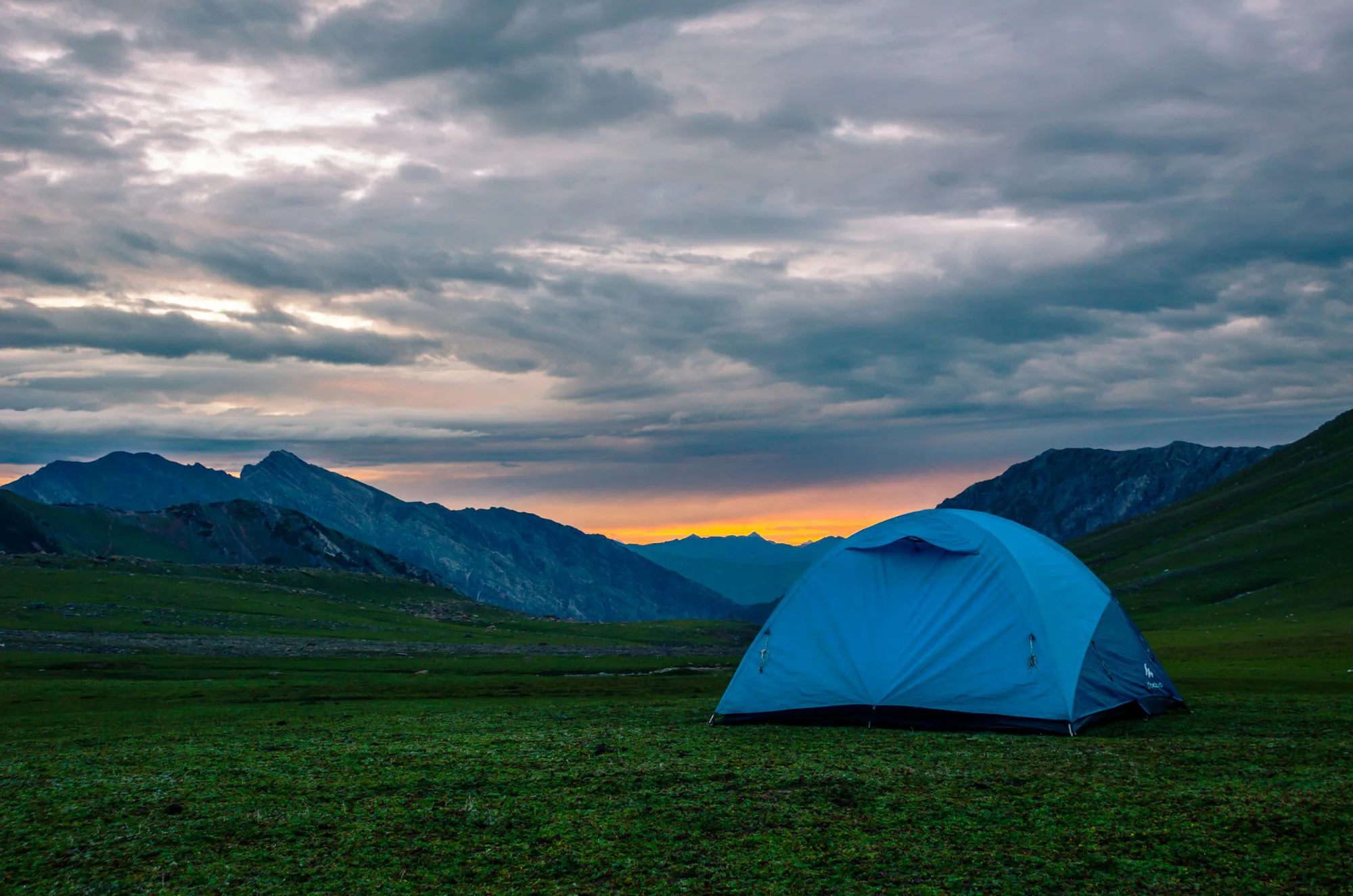 A blue tent in a wide green valley at dusk