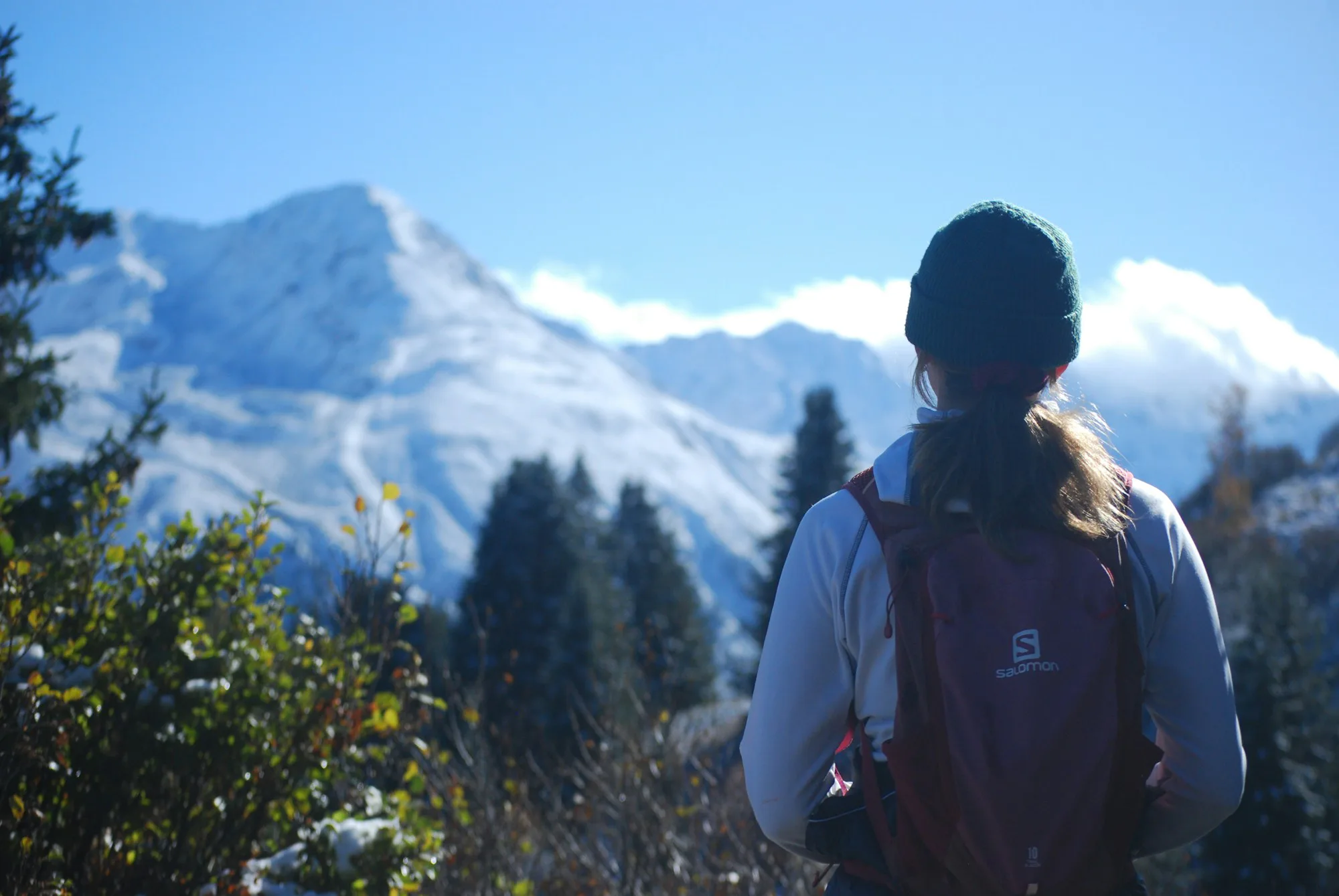 A hiker with a backpack looking at a snowy mountain on a bright day
