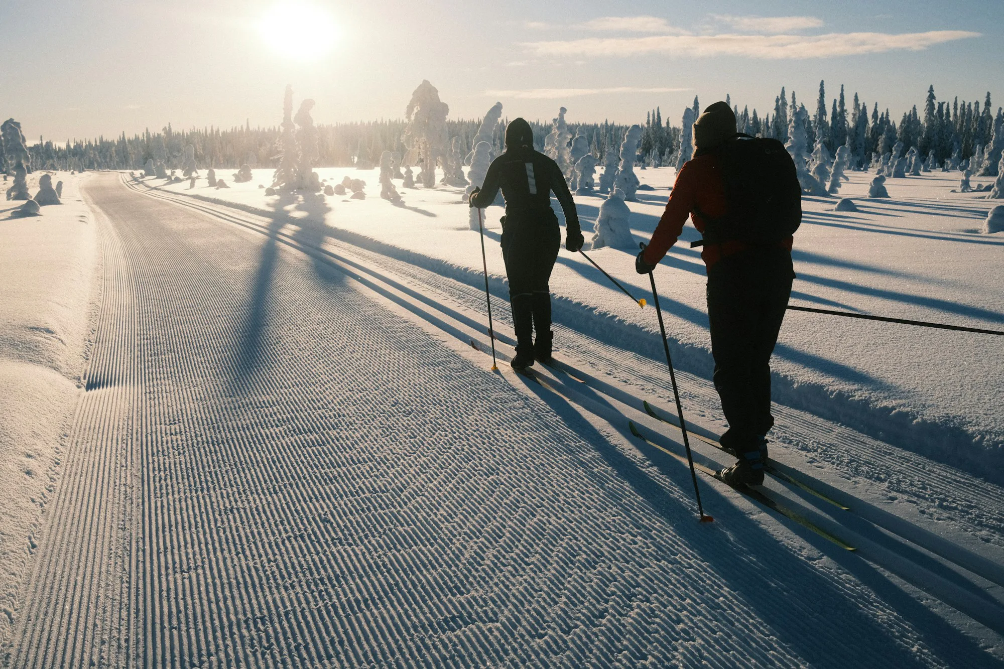 Two cross-country skiers on a groomed trail in low sun
